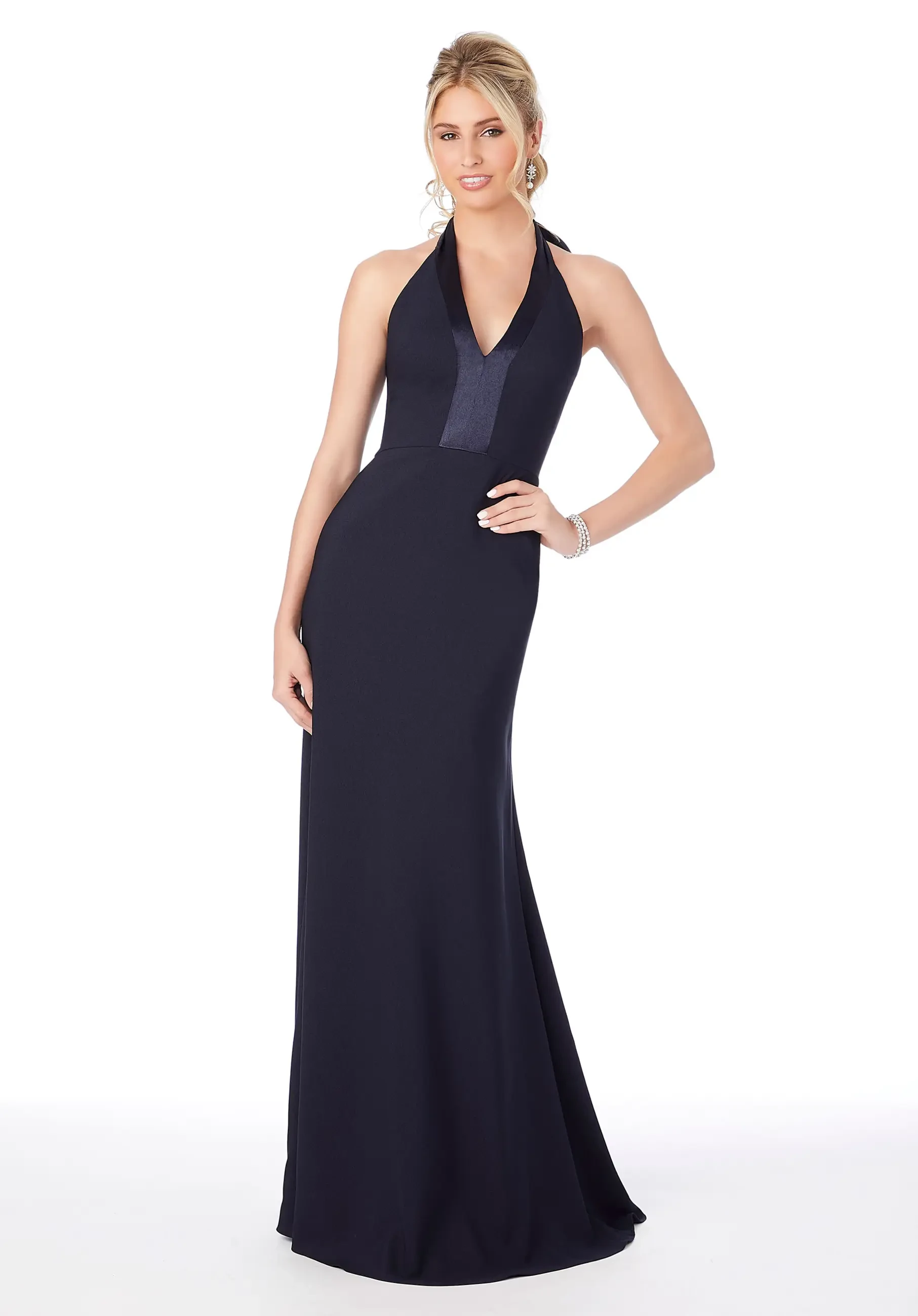 A woman wearing a long, fitted navy blue halter neck dress standing in a pose.