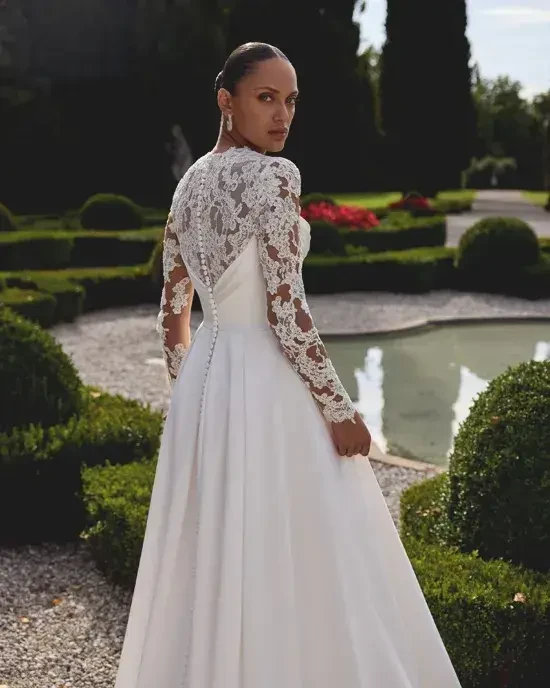 Model is wearing a charmeuse A-line wedding gown with a Queen Anne neckline and corded Alençon lace detailing on the back.