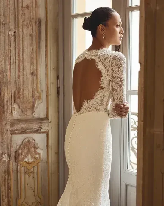 Model is wearing a fit-and-flare wedding gown with allover corded Alençon lace and a keyhole back.