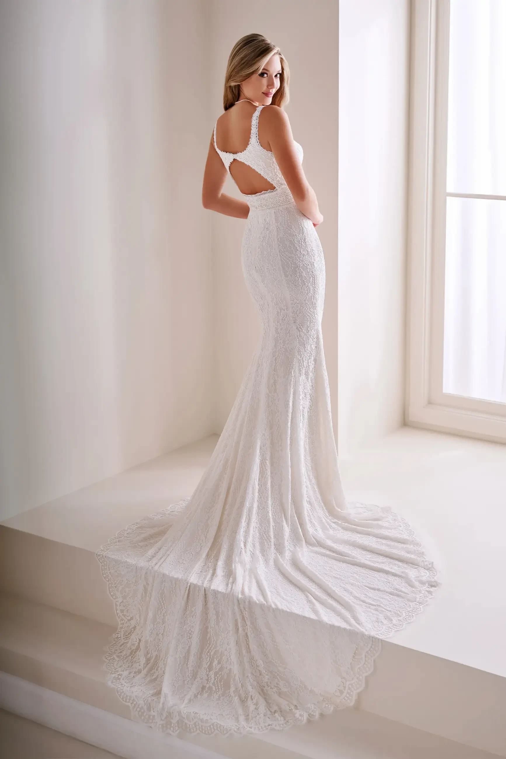 Model is wearing a lace mermaid wedding gown with a scoop neck, separate lace sleeves, and an 80-inch train.