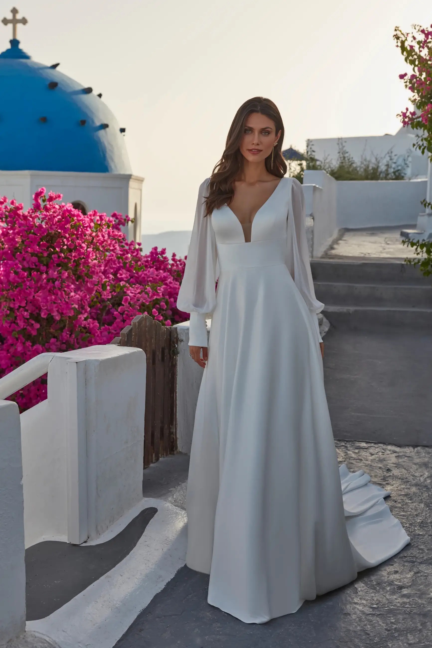 Model is wearing a satin a-line bridal gown with chiffon bishop sleeves by madison james
