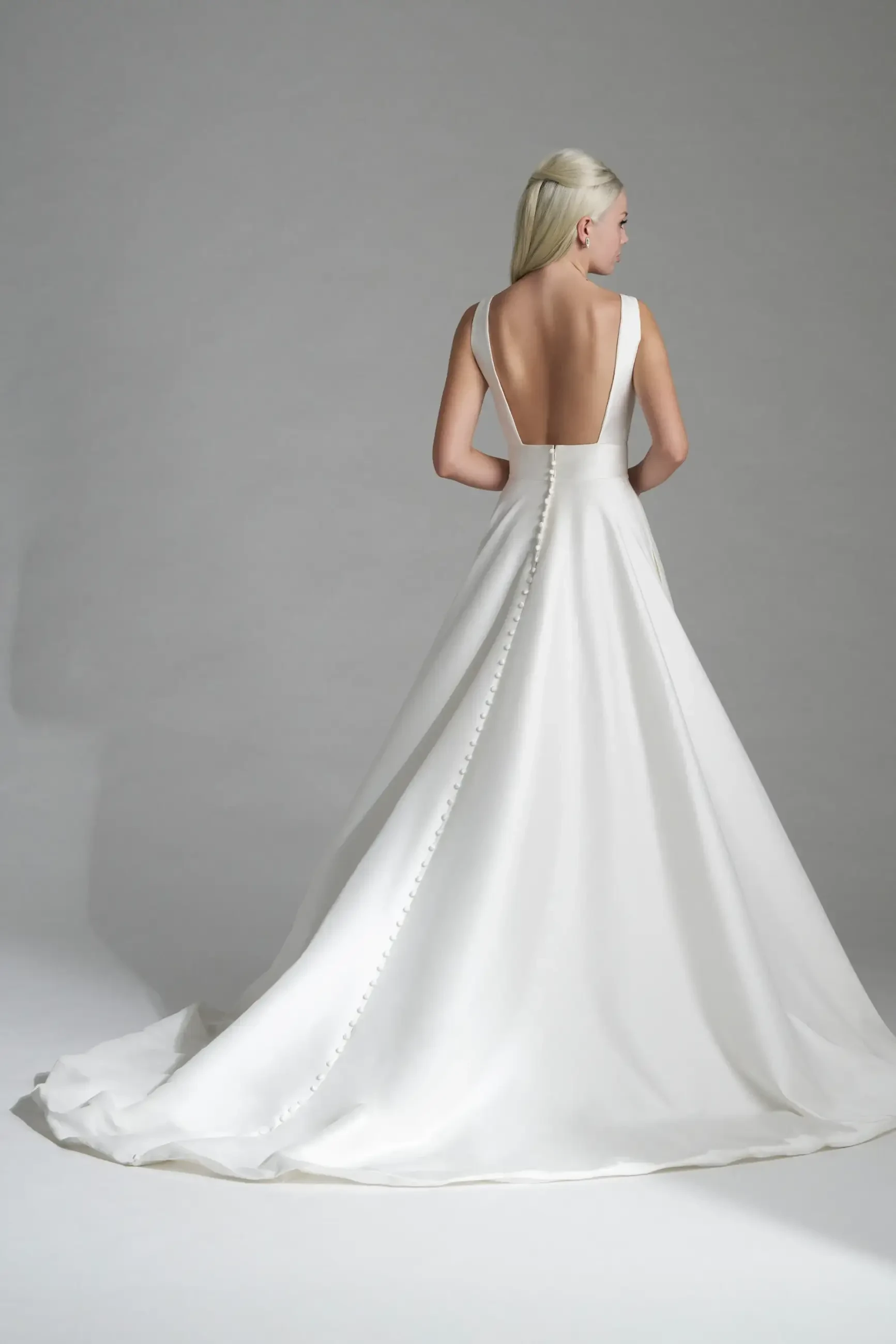 Model is wearing a timeless Mikado A-line gown with a sleeveless bodice, clean silhouette, and a long row of buttons down the back.