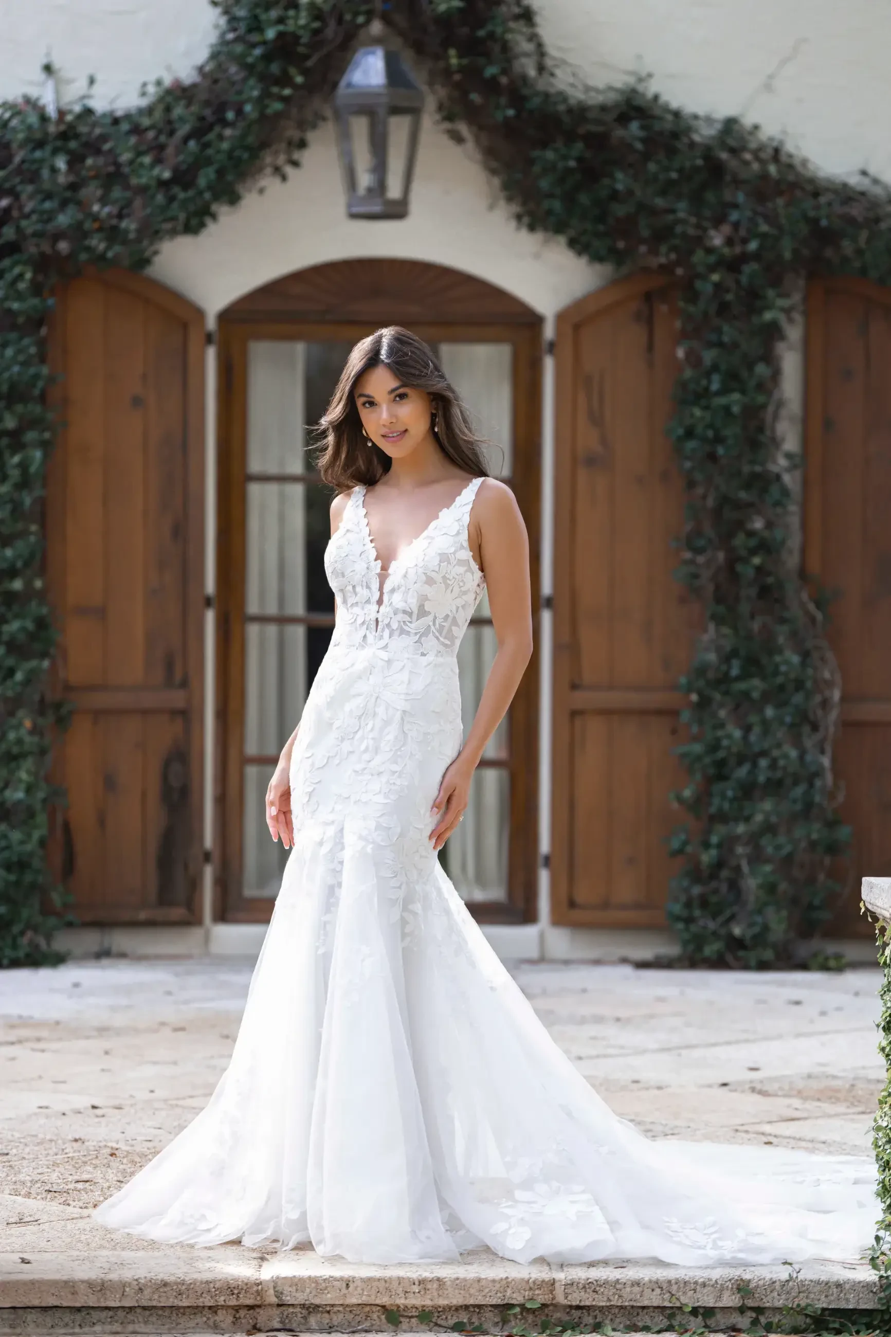 Model is wearing a fit-and-flare gown with a sleeveless V-neckline, sequin lace appliques layered over Chantilly lace and tulle, and a floor-length skirt with a natural waistline.